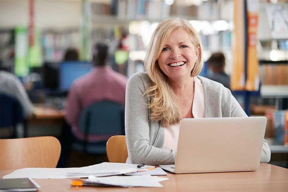 Medelålders kvinna sitter på bibliotek och studerar. 