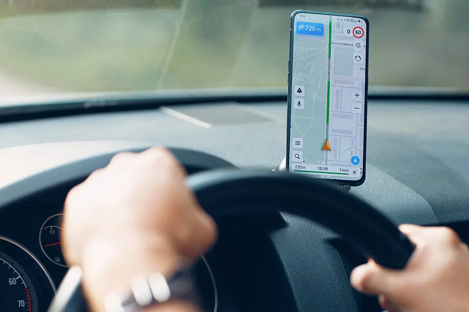 man sitter i bil och kör, har mobiltelefon med kartapp öppen