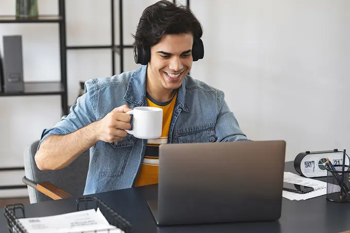 Ung man vid dator med kaffekopp i handen